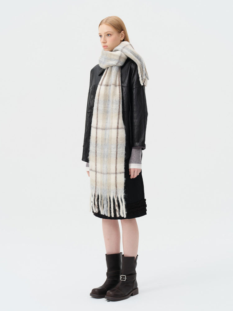 Back view of a model wearing a black jacket, grey top, and a long blue and beige plaid scarf with fringe