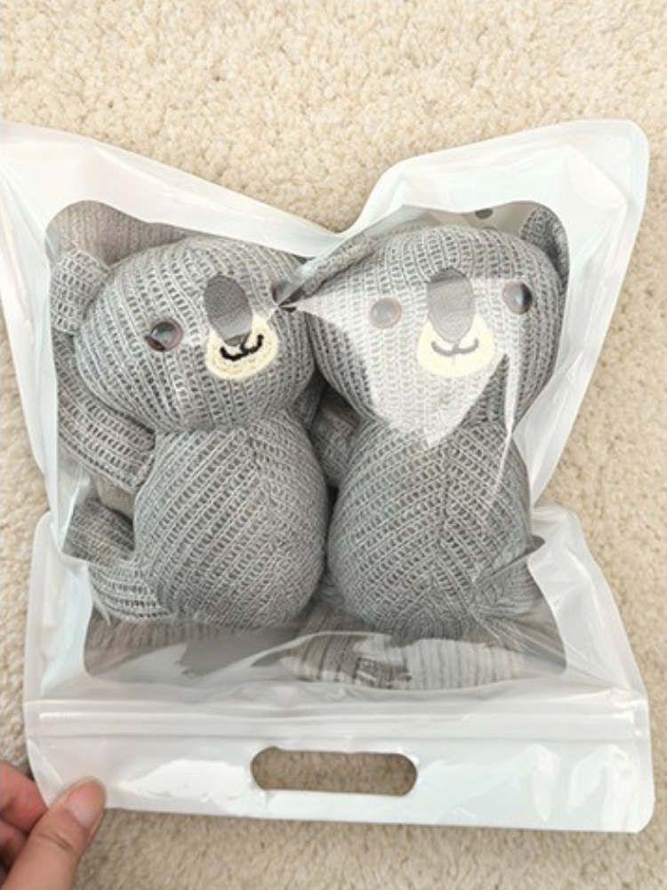 A pair of grey crew socks with 3D koala characters packaged in a clear plastic bag.