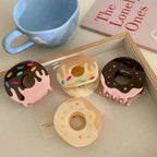 Four donut claw clips are shown in a wooden tray with a blue mug and a pink book in the background.