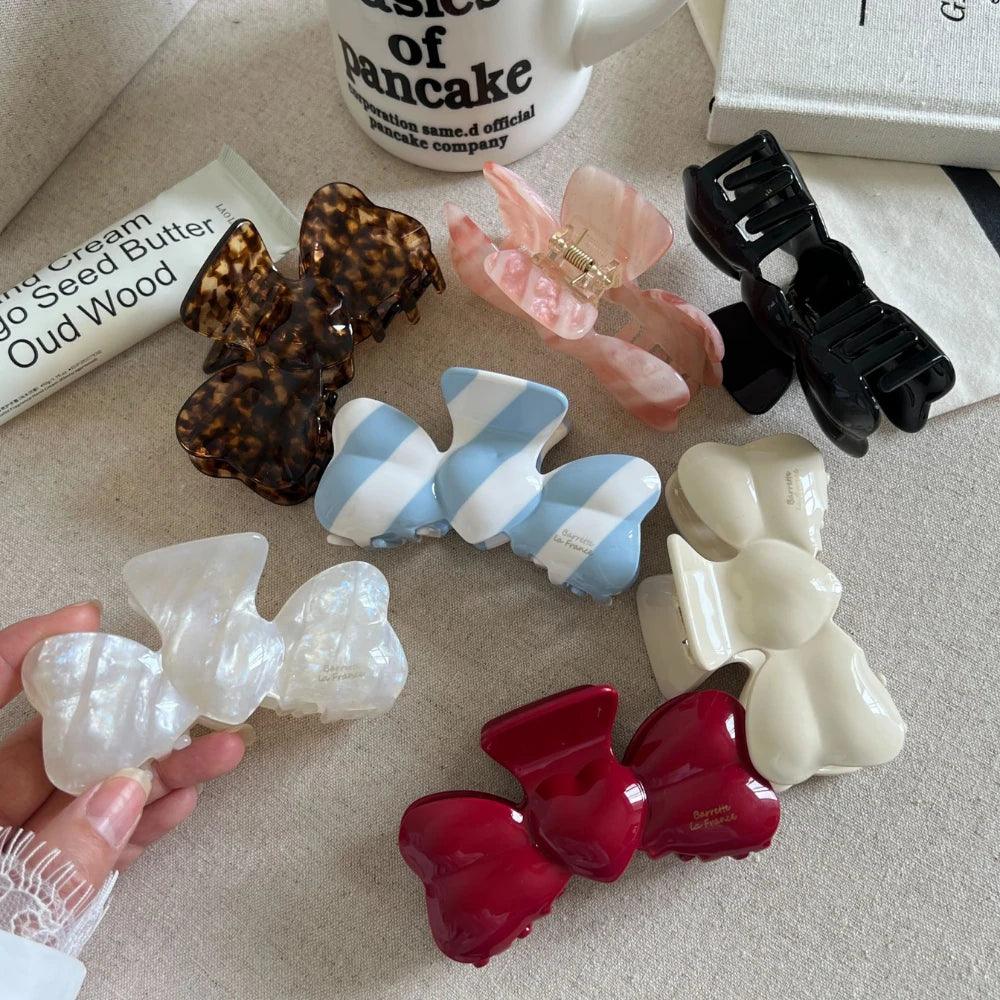 Hand holding a white marbled bow-shaped hair clip, with other hair clips and cosmetic items in the background.