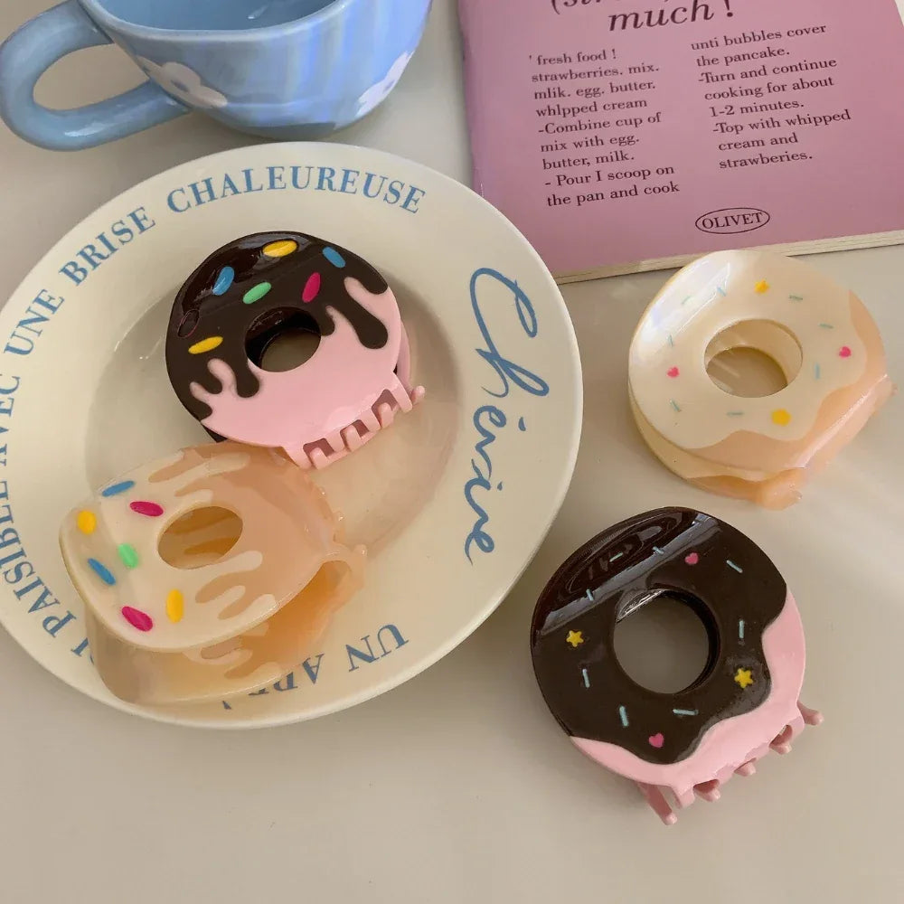 Several donut claw clips are arranged on a decorative plate, with a book and a mug visible in the background.