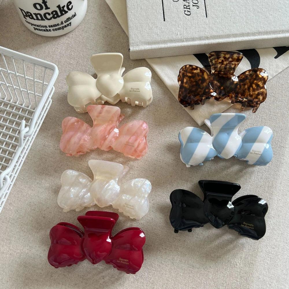 Collection of bow-shaped hair clips in various colors and patterns, including red, black, white, pink, blue and white stripes, and tortoiseshell.