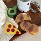 Several novelty hair clips, including a pizza slice, avocado, and peanut, arranged on a wooden tray.