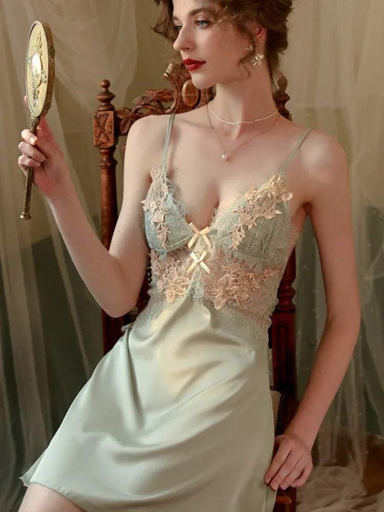 Woman in a light green satin slip dress with lace detailing on the bust, holding a decorative hand mirror.