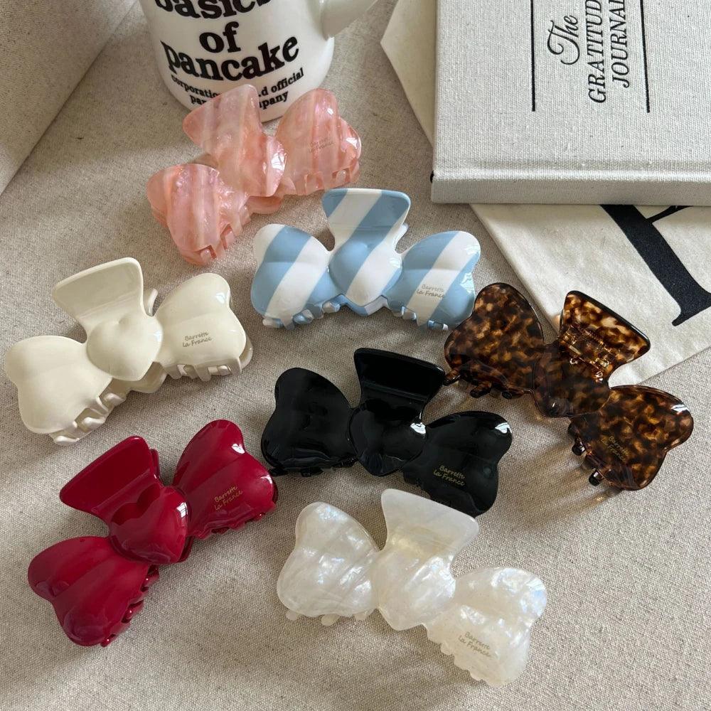 Top-down view of multiple bow-shaped hair clips in different colors and designs arranged on a textured surface.
