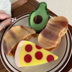 A hand with checkered nail art reaches for a collection of food-themed hair clips, including a pizza slice.