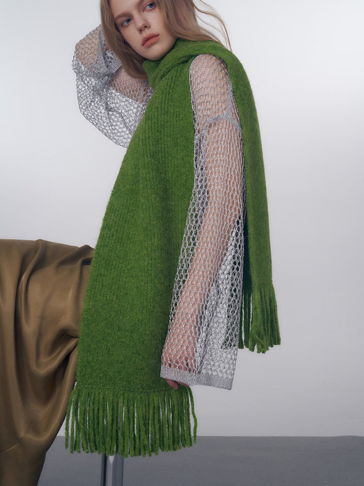 Close-up of a model wearing a green knitted scarf with fringe over a sheer silver top.