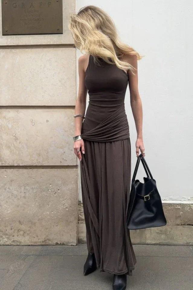 Woman wearing a brown ruched maxi dress with a halter neckline, holding a black handbag. Main image