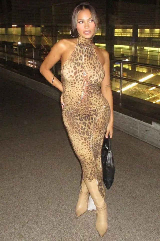 Woman posing in a leopard print halter neck maxi dress with tan boots and a black handbag