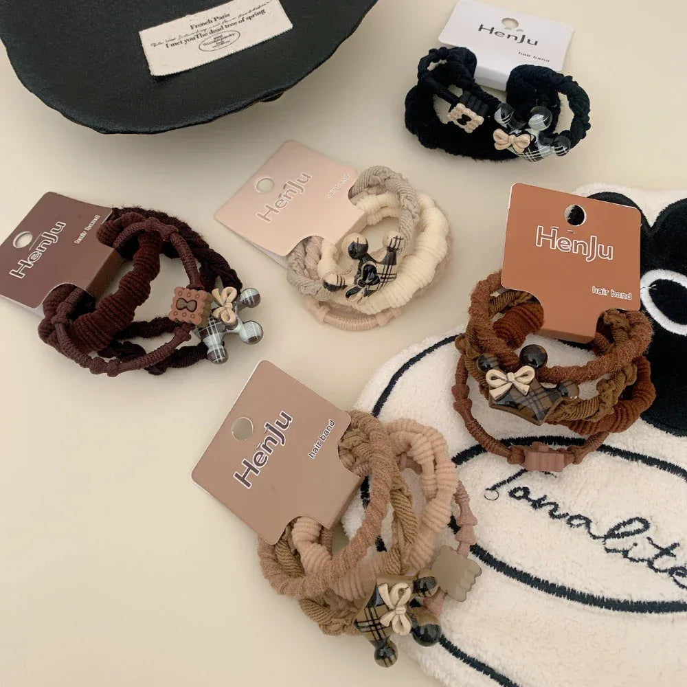 Various Henju hair tie sets displayed on a textured surface, featuring plaid and bow charms