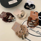 Various Henju hair tie sets displayed on a textured surface, featuring plaid and bow charms