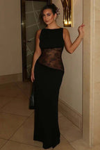 Woman in a floor-length black sleeveless dress with sheer lace waist detailing and a high neckline.