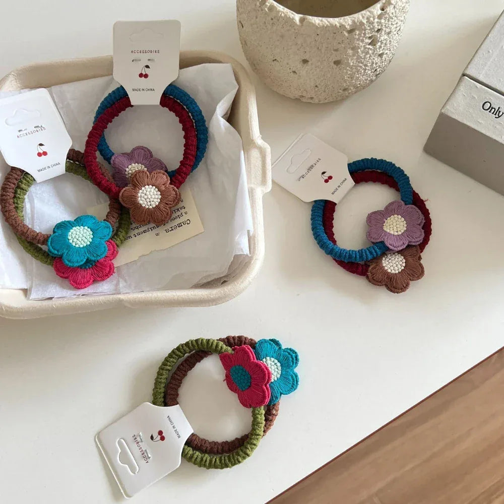 A close-up of crocheted flower hair ties, with some arranged in a white tray and others on a table.