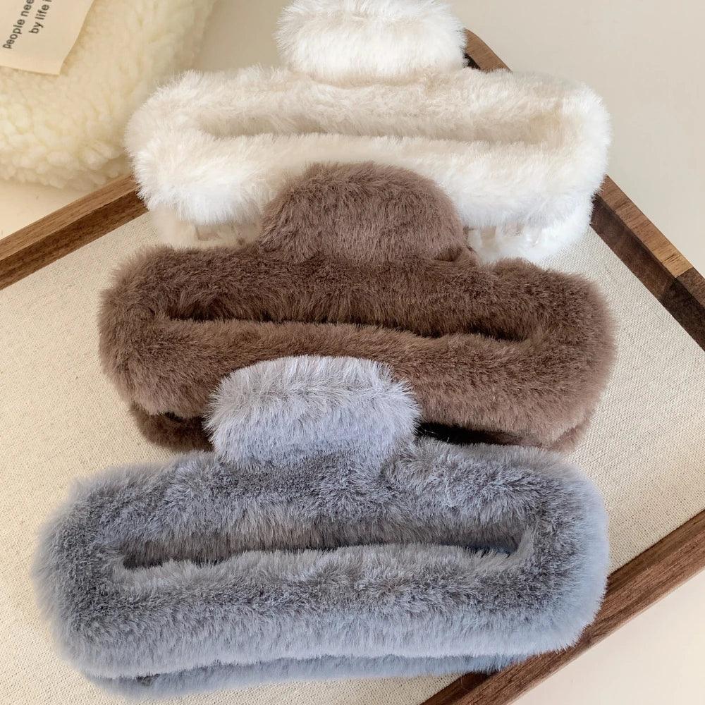 Stack of white, brown, and gray faux fur claw clips on a wooden tray