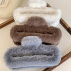 Stack of white, brown, and gray faux fur claw clips on a wooden tray