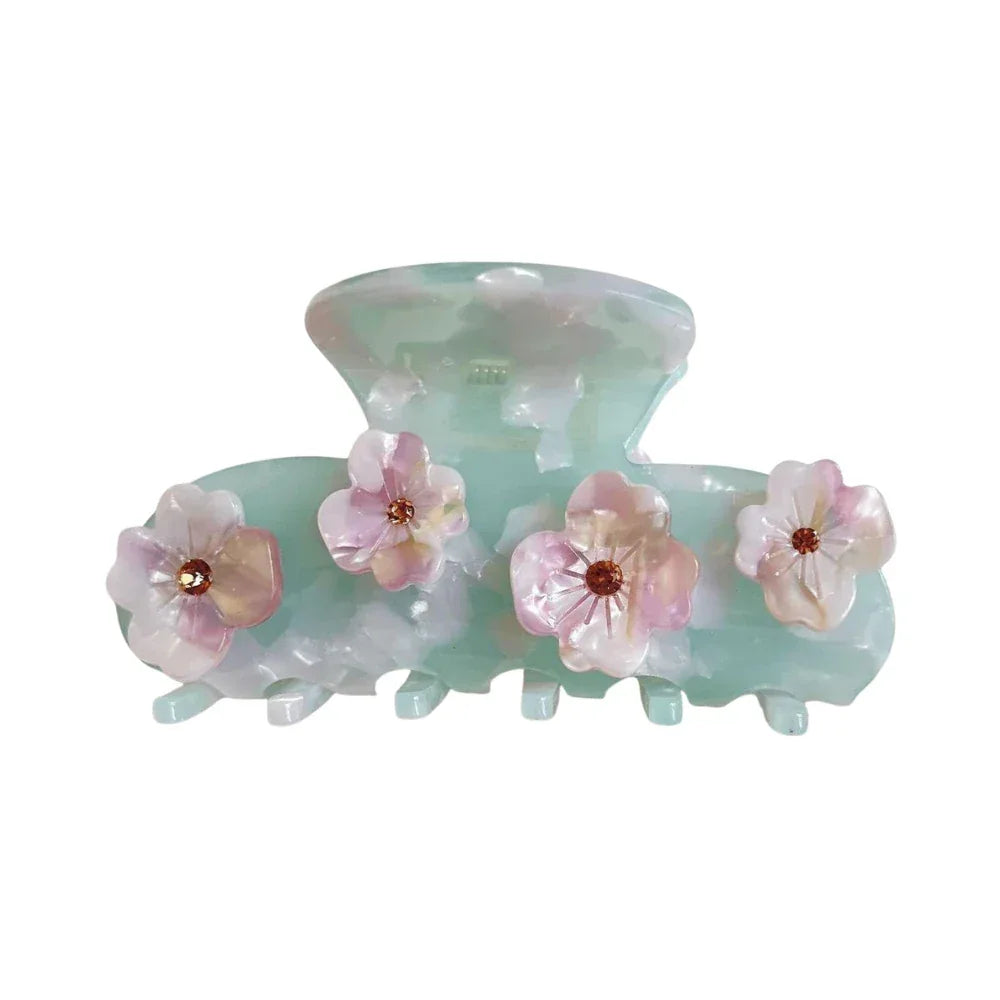 A mint green acetate claw hair clip adorned with four delicate pink and white flowers, each with a small brown gem in the center. Main image