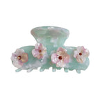 A mint green acetate claw hair clip adorned with four delicate pink and white flowers, each with a small brown gem in the center.