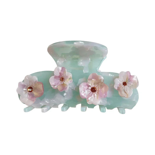 A mint green acetate claw hair clip adorned with four delicate pink and white flowers, each with a small brown gem in the center.