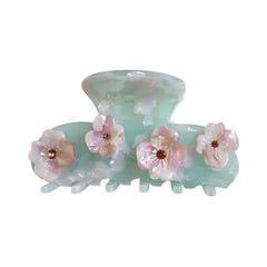 A mint green acetate claw hair clip adorned with four delicate pink and white flowers, each with a small brown gem in the center.