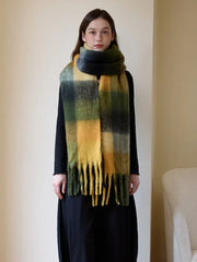 Full body shot of a woman modeling a warm, plaid scarf with fringe accents.