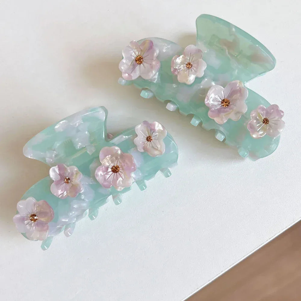 Two mint green acetate claw hair clips with floral embellishments arranged on a white surface.