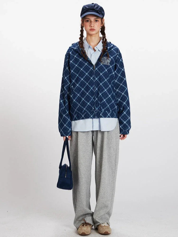 Model wearing a blue plaid hooded jacket, light blue collared shirt, grey sweatpants, and a navy blue cap, holding a navy blue handbag. Main image