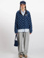 Model wearing a blue plaid hooded jacket, light blue collared shirt, grey sweatpants, and a navy blue cap, holding a navy blue handbag.