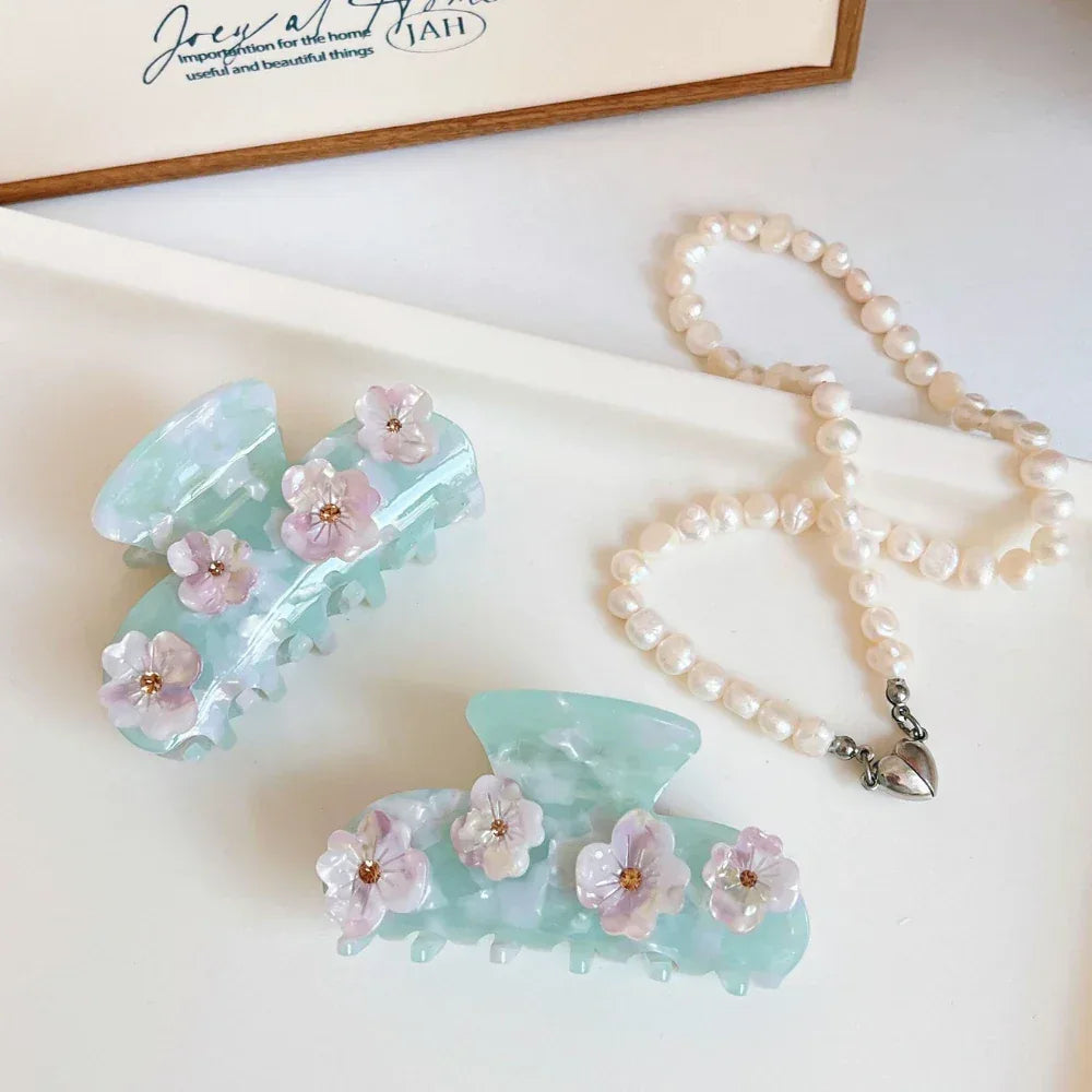 Two mint green acetate claw hair clips with floral embellishments and a strand of pearls on a white surface.