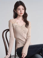 Woman sitting on a chair wearing a beige ribbed knit cardigan with lace trim and a v-neck, paired with dark wash jeans.