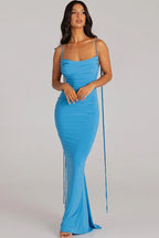 Woman wearing a long blue ruched dress with spaghetti straps and an open back