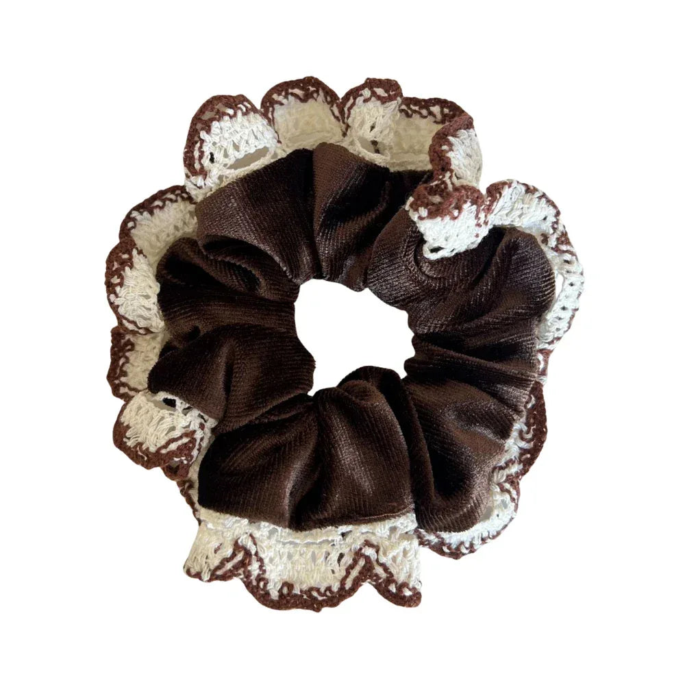 A brown velvet scrunchie with white and brown crocheted lace trim is shown against a white background.