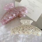 Two marbled claw clips, one pink and one cream, with rhinestones, placed on a fluffy white surface next to a card with text