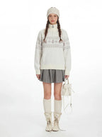 Model wearing a white knit sweater with a Fair Isle pattern and snowman graphic, paired with a grey pleated skirt, white knee-high socks, and cream ankle boots.