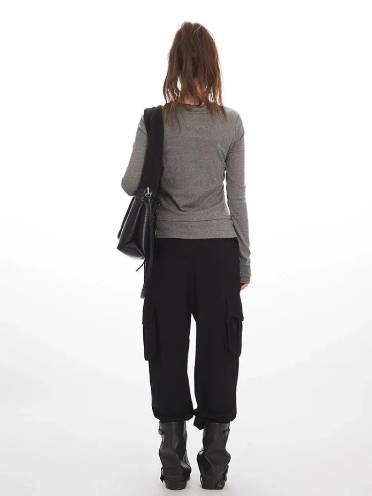 Back view of a woman wearing a grey long-sleeved shirt with a layered hem and black cargo pants.