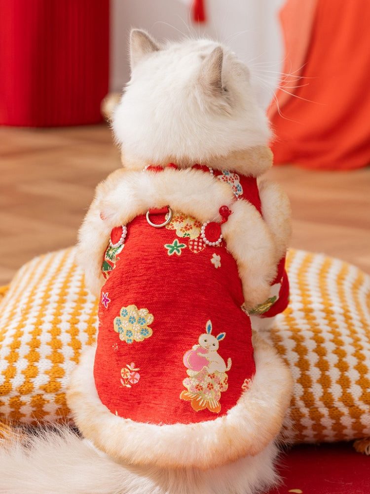 The back of a white cat wearing a red traditional Chinese jacket with embroidered floral patterns and faux fur trim, showing a rabbit design on the back.