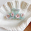 A mint green acetate claw hair clip with floral embellishments resting inside a white shell-shaped dish.