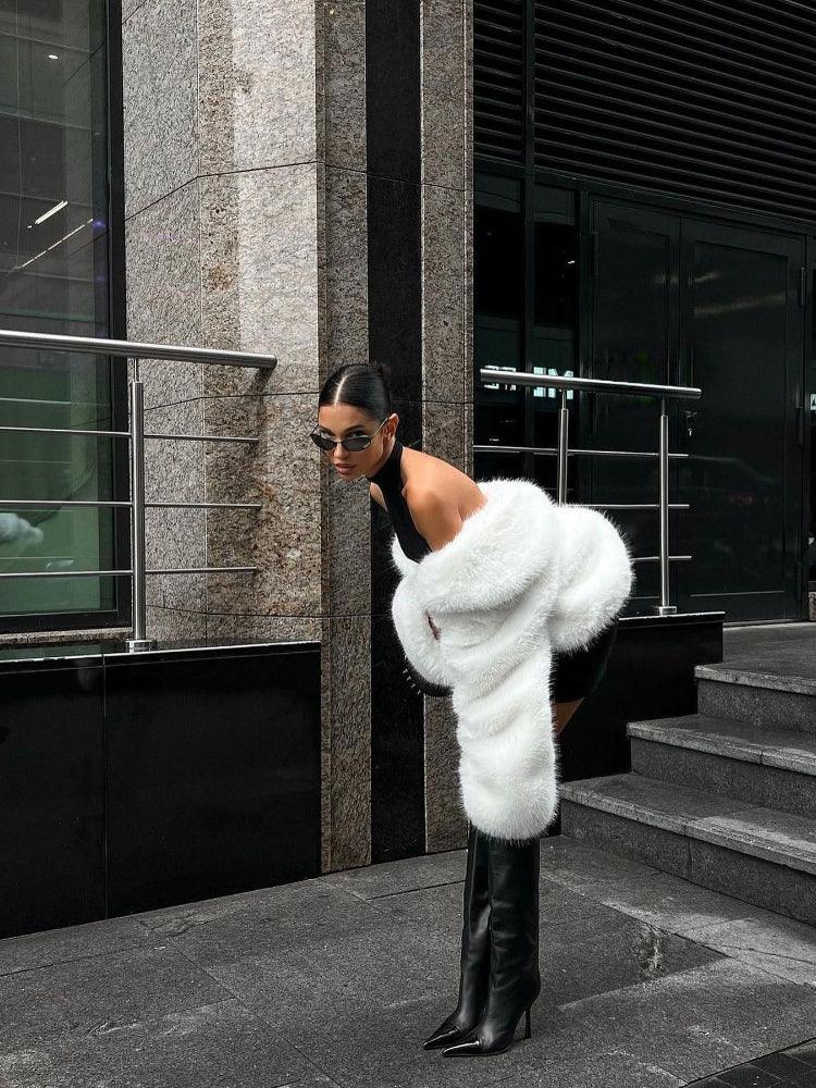 woman bending over in a black dress with a white faux fur jacket and black boots