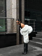 woman bending over in a black dress with a white faux fur jacket and black boots