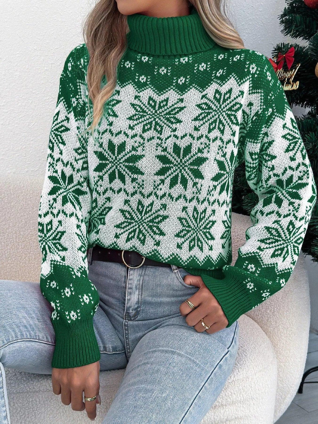 Woman sitting on a couch wearing a green and white snowflake print turtleneck sweater
