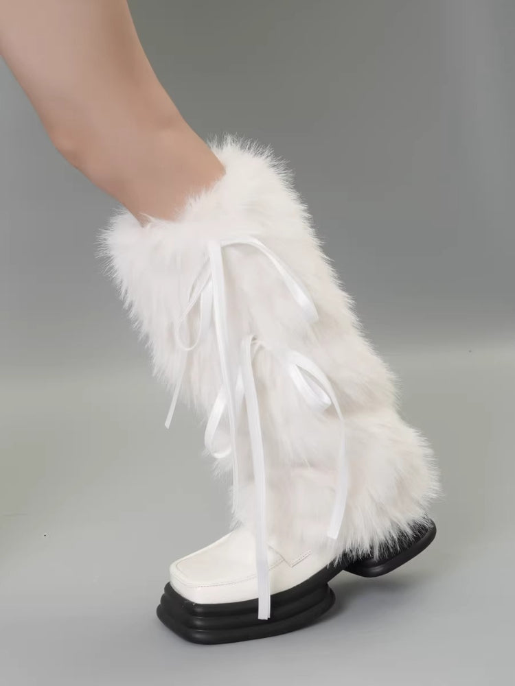 A single leg wearing a white faux fur leg warmer with white ribbon ties, partially obscuring a white shoe.