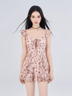 Front view of a woman in a pink floral print mini dress with ruffle trim and flutter sleeves, with her hair blowing.