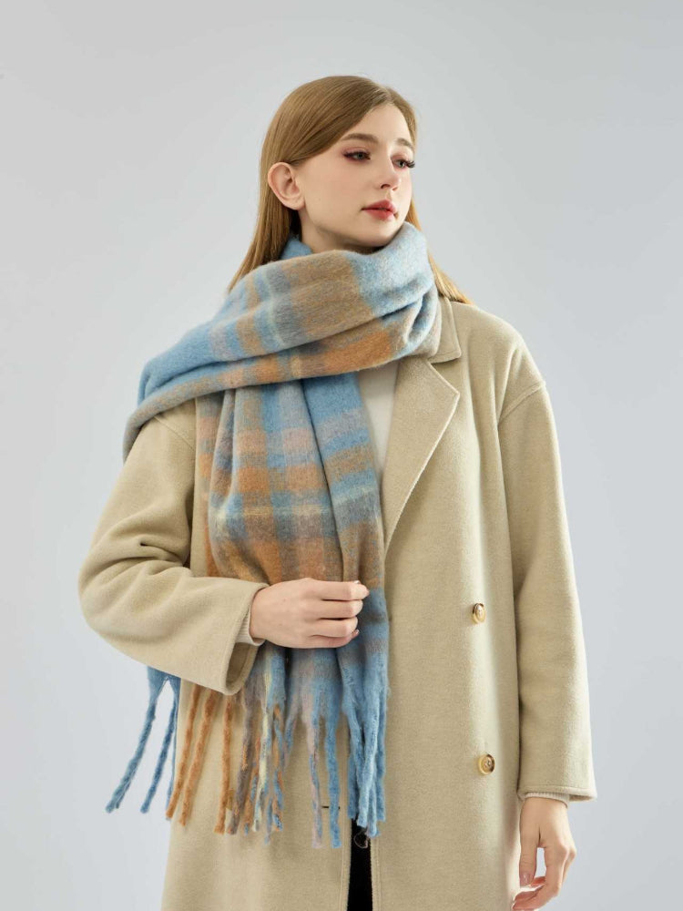 Woman wearing a beige coat and a blue and tan plaid scarf draped over her shoulders.