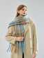 Woman wearing a beige coat and a blue and tan plaid scarf draped over her shoulders.