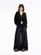 Full body shot of a model wearing a black V-neck knit cardigan with an embroidered dachshund detail, a black tank top, and dark wash wide-leg jeans, with an ID badge holder around her neck.