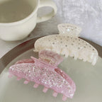 Two marbled claw clips, one pink and one cream, with rhinestones, placed on a plate next to a mug