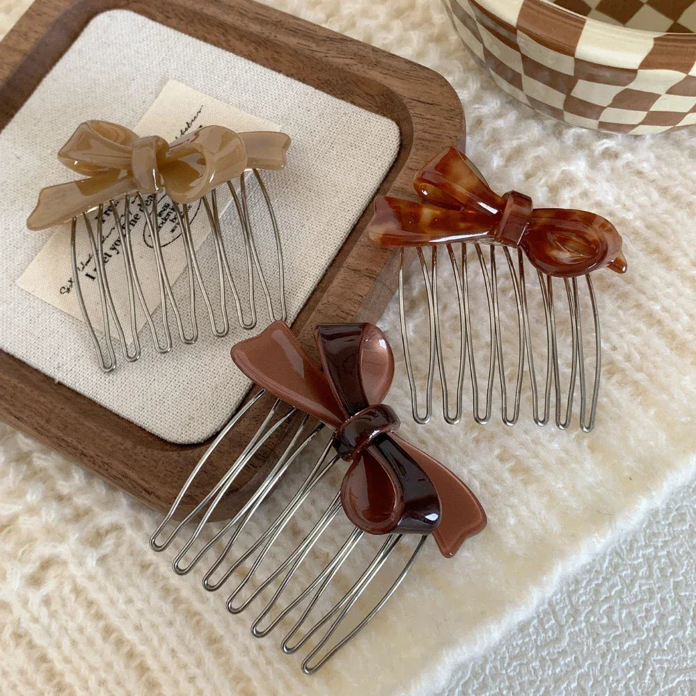 Three bow hair combs in beige, tortoiseshell, and brown arranged on a white textured surface with wooden accents.