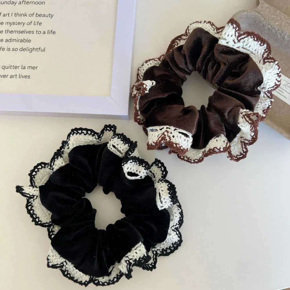 Two scrunchies, one brown and one black, both with white and brown crocheted lace trim, are displayed on a white surface next to a framed piece of text.