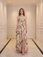 Woman wearing a cream-colored floral print maxi dress with spaghetti straps and a thigh-high slit, standing in a hallway.