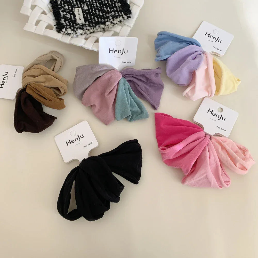A collection of colorful scrunchies arranged on a white surface, including pinks, blues, purples, yellows, browns, and black.