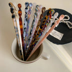 A collection of various patterned hair sticks displayed upright in a mug.